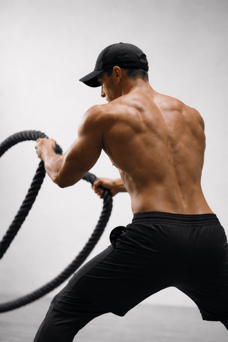 Muscular man in black shorts and cap using battle ropes for fitness workout