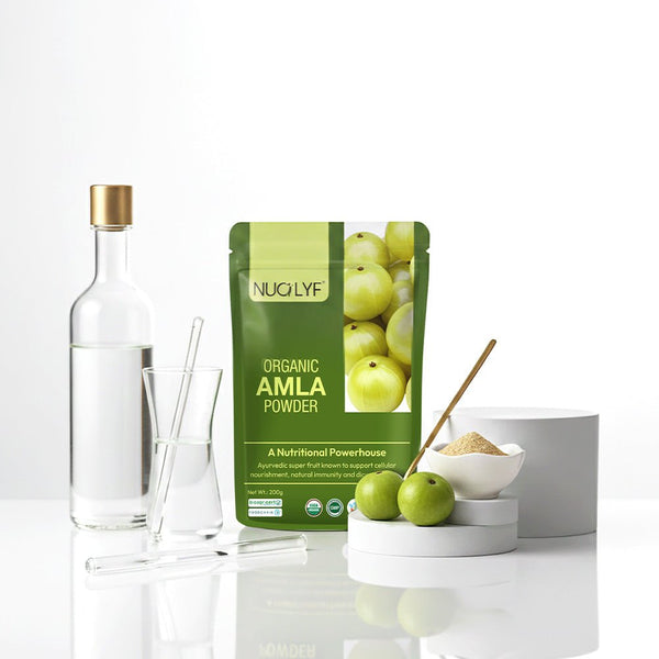 Organic amla powder pouch with fresh amla fruit, glassware, and powder in a bowl on a white surface