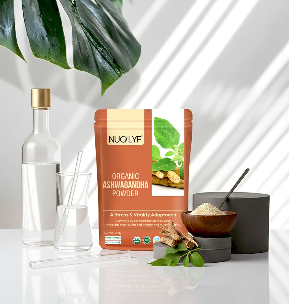 Organic ashwagandha powder pouch with glassware, leaves, and ashwagandha root on white table.