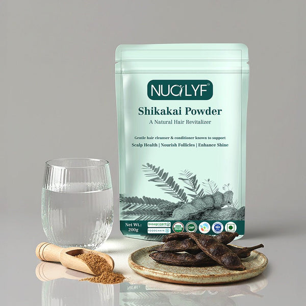 Shikakai powder pouch with glass of water, wooden scoop of powder, and dried shikakai pods on a plate